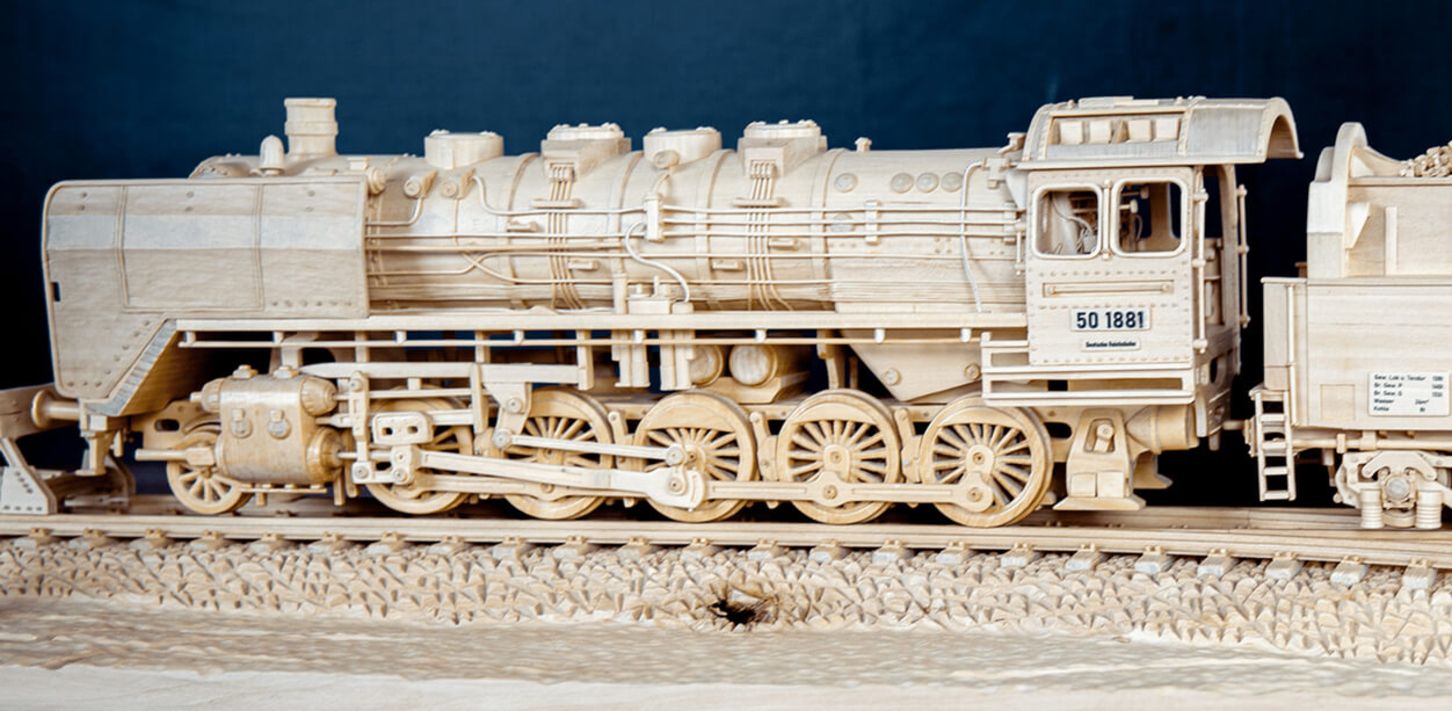 Detailliertes Holzmodell einer Dampflokomotive mit Tender auf Schienen.